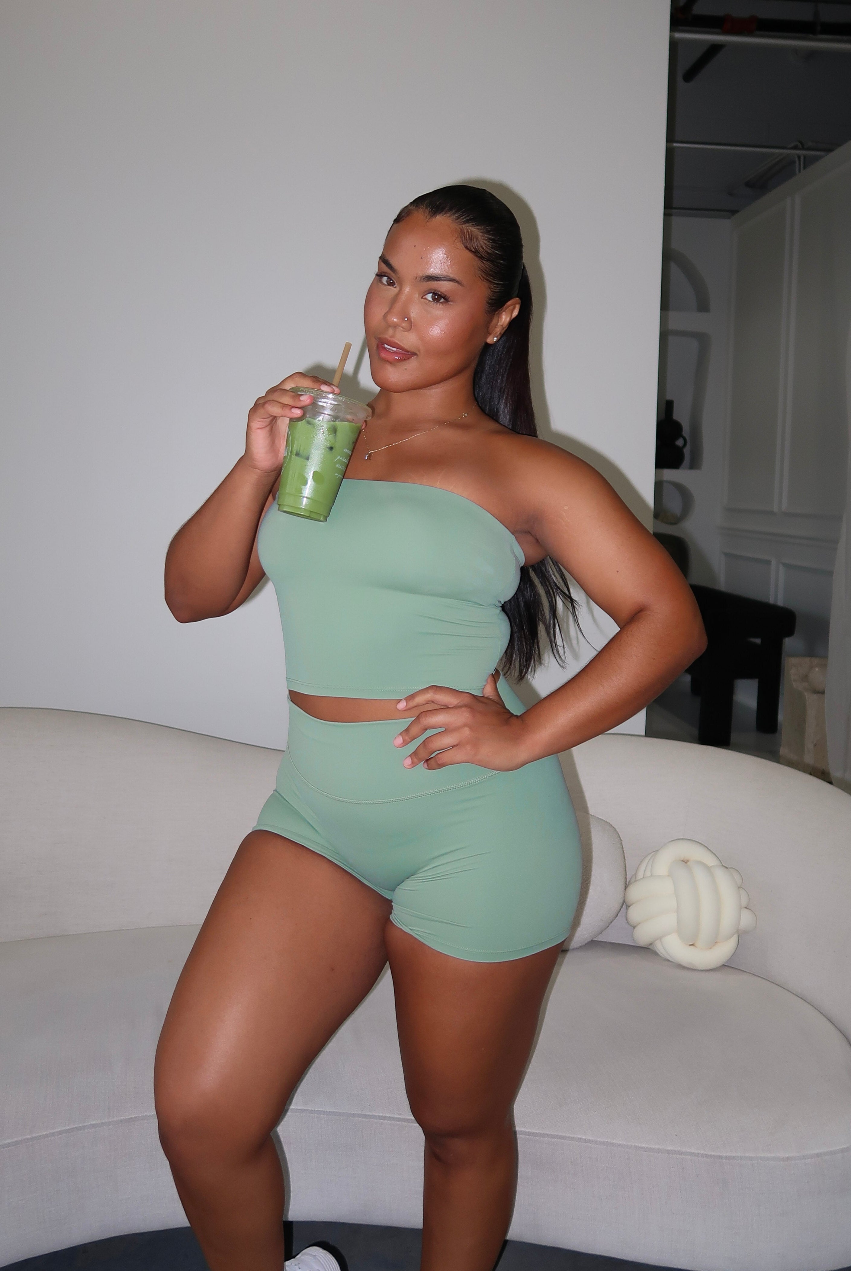 Woman in green athletic wear holding a drink in a modern indoor setting