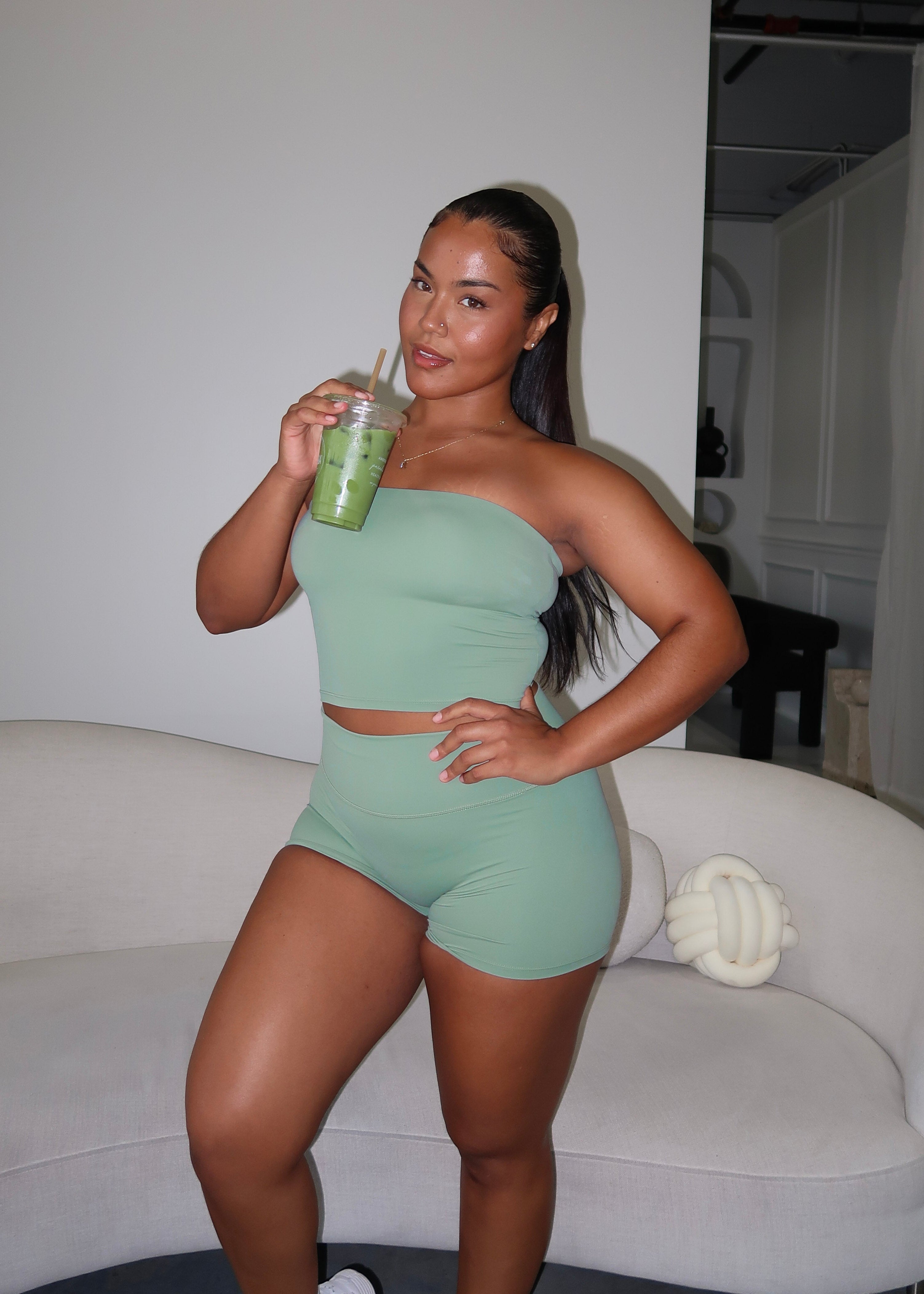 Woman in green athletic wear holding a drink in a modern indoor setting