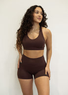 Woman wearing a brown sports bra and shorts set against a plain background