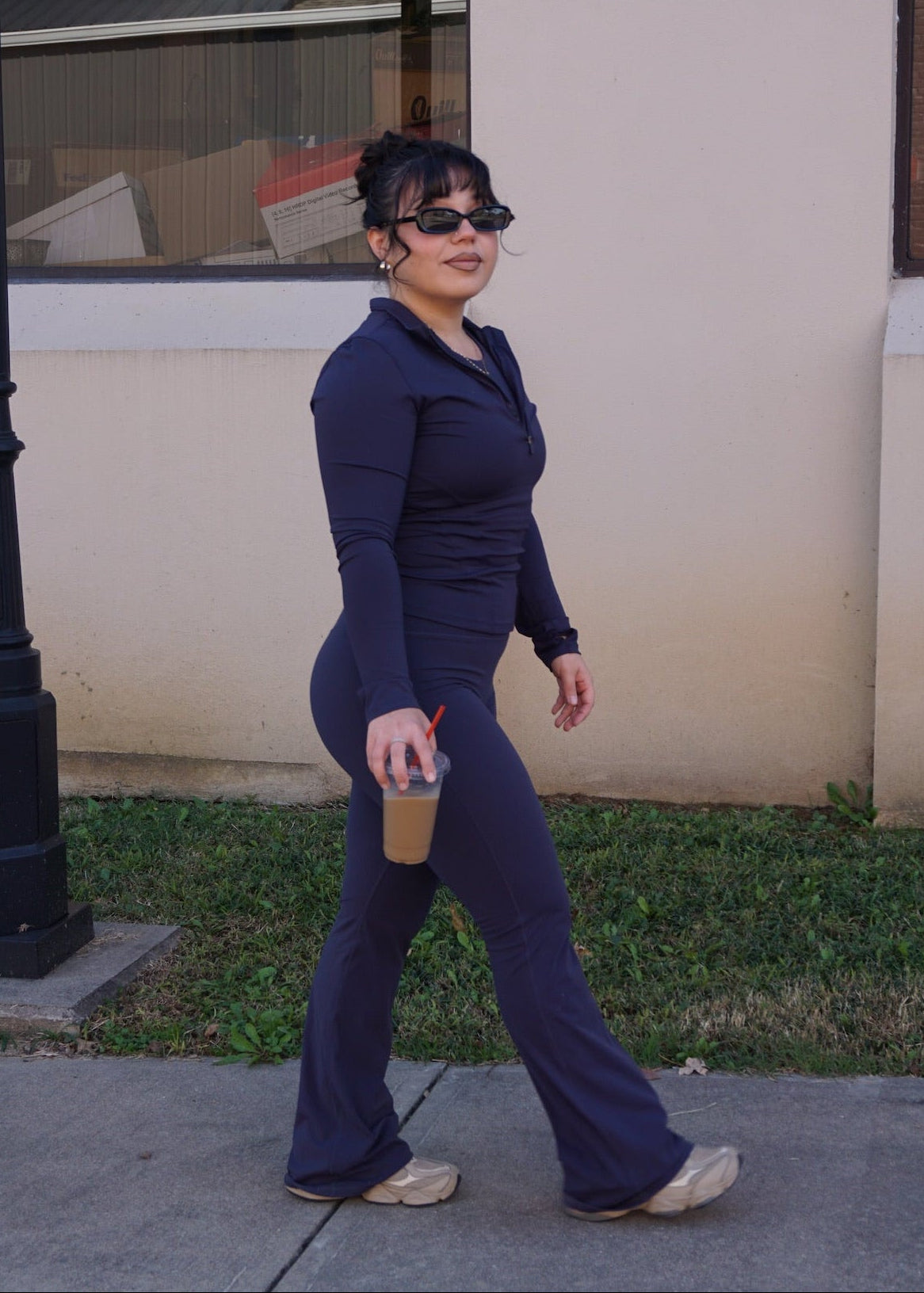 Woman in navy outfit walking on a sidewalk with a building in the background